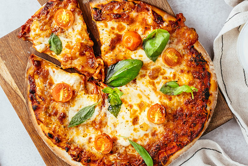 A full sized pizza with basil leaves and tomatoes on top of a wooden board